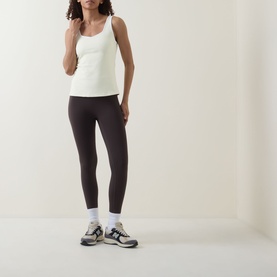 Model wearing Sweaty Betty Butterscotch Yellow tank top with dark leggings and grey trainers with white ankle socks.