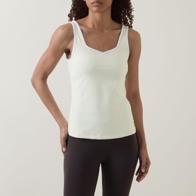 Model wearing Sweaty Betty tank in Butterscotch Yellow with sweetheart neckline, styled with dark brown leggings.