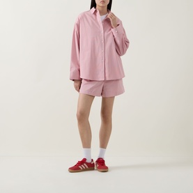 Model wearing Sweaty Betty Summer Stripe Shirt in Pink White Stripe, styled with matching pink shorts and red trainers.