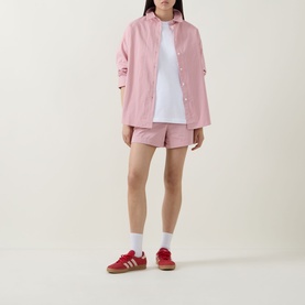 Model wearing Sweaty Betty Summer Stripe Shirt in Pink White Stripe, styled with matching pink shorts and red Adidas trainers.