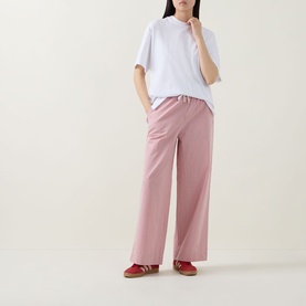Model wearing pink wide-leg trousers with elasticated waist, styled with a white oversized T-shirt and red trainers