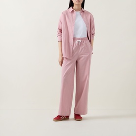 Model wearing pink wide-leg drawstring trousers styled with matching pink shirt, white tee, and red trainers