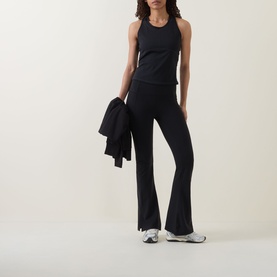 Model wearing Sweaty Betty black tank top, styled with matching black flared trousers, white trainers, holding black jacket