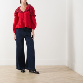 Model wearing Damson Madder red cotton blouse with ruffle collar and puff sleeves, styled with wide-leg navy jeans and black flats.