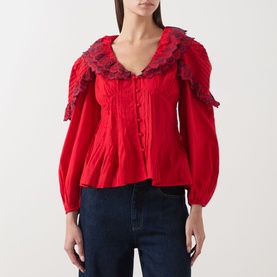 Model wearing Damson Madder red cotton blouse with oversized frill collar, lace trim, puff sleeves and button-front detail, styled with blue jeans.