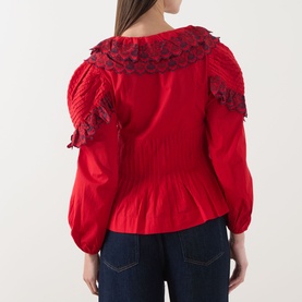 Model wearing Damson Madder red cotton blouse, rear view, showing ruffled lace collar, puff sleeves, and smocked waist, styled with dark jeans.