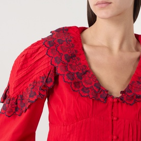 Model wearing Damson Madder red cotton blouse, featuring navy floral lace oversized collar and ruffled sleeves, close-up detail view.