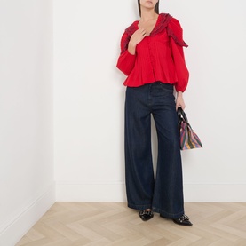Model wearing Damson Madder red cotton blouse with ruffle V-neckline and balloon sleeves, styled with wide-leg navy trousers and black flats.