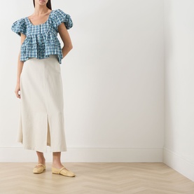 Model wearing Damson Madder blue gingham cotton blouse with puff sleeves and ruched detail, styled with cream midi skirt and yellow loafers.