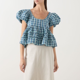 Model wearing Damson Madder blue check cotton blouse with puff sleeves, smocked bodice and tiered hem, styled with a cream midi skirt.