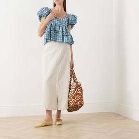Model wearing Damson Madder blue gingham cotton blouse with puffed sleeves and square neck, styled with cream midi skirt and yellow mules.