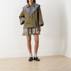 Model wearing Damson Madder olive cotton coat with blue check lapels, styled with a check mini skirt and black loafers