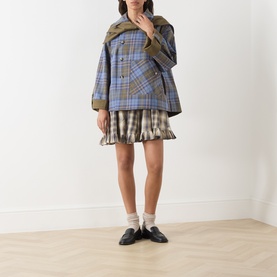Model wearing Damson Madder olive check cotton coat, styled with a pleated mini skirt, white socks and black loafers