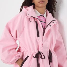 Model wearing Damson Madder pink oversized coat with black contrast trim, drawstring waist, and funnel neck with snap fastening detail.