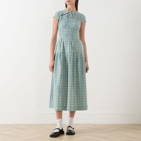 Model wearing Damson Madder multi check cotton midi dress with bow neckline, cap sleeves and tiered skirt, styled with black loafers
