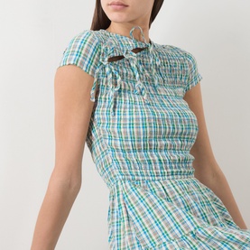 Model wearing Damson Madder multi-coloured check cotton dress with smocked bodice, cut-out detail, and frilled neckline.