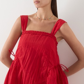 Model wearing Damson Madder red crinkle mini dress with ruched straps and tie sides, styled with a delicate beaded choker necklace.