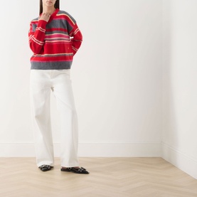 Model wearing Damson Madder pink/red stripe merino wool knit jumper, styled with white wide-leg trousers and black flat shoes.