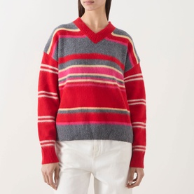 Model wearing Damson Madder pink and red stripe merino wool V-neck sweater, styled with white trousers.