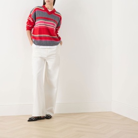 Model wearing Damson Madder pink/red stripe merino wool knit, styled with white wide-leg trousers and black loafers.