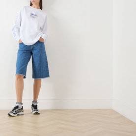 Model wearing Damson Madder white long-sleeve cotton T-shirt, styled with mid-blue denim bermuda shorts and chunky trainers.