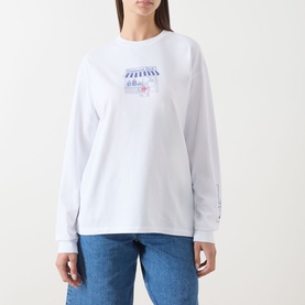 Model wearing Damson Madder white long-sleeve cotton T-shirt with small graphic print on chest, styled with blue jeans.