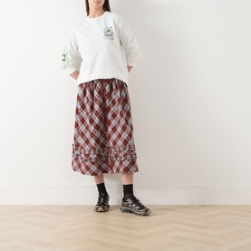 Model wearing Damson Madder Plant Patch Pals T-Shirt in white with long sleeves, styled with red gingham midi skirt and black trainers.