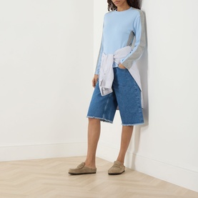 Model wearing Damson Madder blue cotton longline T-shirt, styled with denim shorts, white shirt tied at waist and khaki loafers.