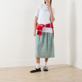 Model wearing Damson Madder white cotton T-shirt, styled with green check midi skirt, red knotted jumper and black mary jane flats.