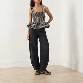 Model wearing Damson Madder yellow check peplum cami top with wide-leg dark grey jeans and chunky trainers