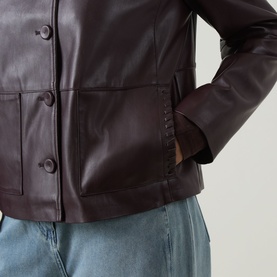 Model wearing Elena Miro jacket in Must, close-up of patch pockets, button fastening, and cuff detail, styled with light blue jeans.