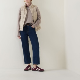 Model wearing Gant Logo Down-Filled Gilet in beige, styled with a striped top, dark blue jeans and burgundy trainers