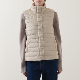 Model wearing Gant Logo Down-Filled Gilet in beige, styled with grey knit sleeves and blue jeans. Stand-up collar, quilted finish