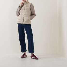 Model wearing Gant Logo Down-Filled Gilet in beige with stand-up collar, styled with grey knit, dark jeans and burgundy trainers