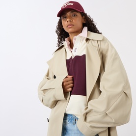 Model with Gant Raised Graphic Logo Baseball Cap in purple, six-panel peak visor style, styled with beige trench coat and burgundy polo shirt.
