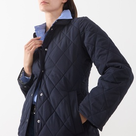 Model wearing Gant Quilted Fitted Jacket in blue, showing diamond quilt pattern and snap button fastening, styled with a blue striped shirt