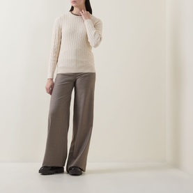Model wearing Gant Shield Logo Cable Knit Sweater in beige with crew neck and cable knit detail, styled with wide-leg taupe trousers.