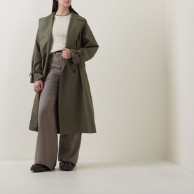 Model wearing Gant Shield Logo Cable Knit Sweater in beige, styled with an olive trench coat and wide-leg grey trousers.