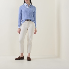 Model wearing Gant Shield Logo Cable Knit Sweater in Misty Lavender over a shirt, styled with white trousers and brown loafers.