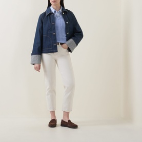 Model wearing Gant Shield Logo Cable Knit Sweater in Misty Lavender, styled with white trousers, denim jacket and brown loafers.