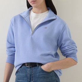 Model wearing Gant Shield Logo Half-Zip Sweatshirt in lavender with funnel neck and half-zip, styled with white tee and blue jeans.