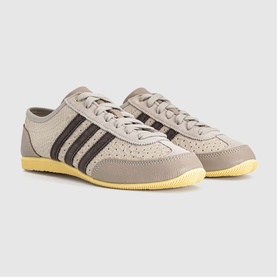 Adidas trainers in wonder beige with dark brown three-stripe detail, perforated leather upper and yellow rubber cupsole.