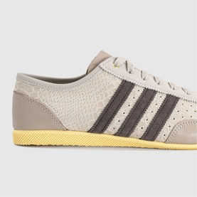 Adidas trainer in wonder beige and dark brown, textured upper with three dark brown stripes and distinctive yellow rubber sole.