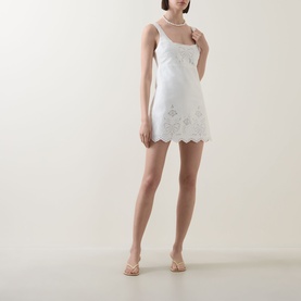 Model wearing LOVESHACKFANCY Fable Cut-Out Mini Dress in Moonbeam, white scalloped hem, floral eyelet embroidery, styled with nude heeled sandals