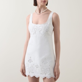 Model wearing LOVESHACKFANCY Fable Cut-Out Mini Dress in white, with square neckline, bow and floral eyelet embroidery, scalloped hem; styled with