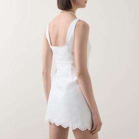 Model wearing LOVESHACKFANCY Fable Cut-Out Mini Dress in Moonbeam white, back view showing wide straps, fitted silhouette and scalloped eyelet hem.