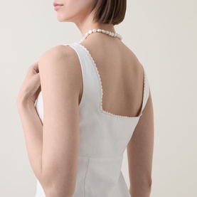 Model wearing LOVESHACKFANCY Fable Cut-Out Mini Dress in Moonbeam, showing open back with scalloped eyelet trim detail, styled with a pearl necklace.