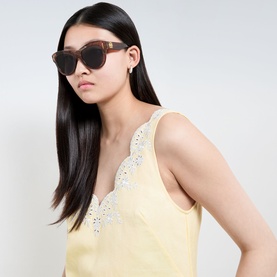 Model with Loewe Anagram Round Sunglasses in Havana, round acetate frames with gold-tone hardware, styled with yellow lace-trim cami top