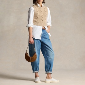 Model carrying Polo Ralph Lauren Cinnamon/Cuoio shoulder bag, styled with cable-knit vest, white shirt, blue jeans and white trainers.