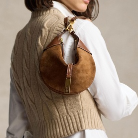 Model carrying Polo Ralph Lauren shoulder bag in cinnamon suede with gold hardware, styled with white shirt and cable-knit vest.